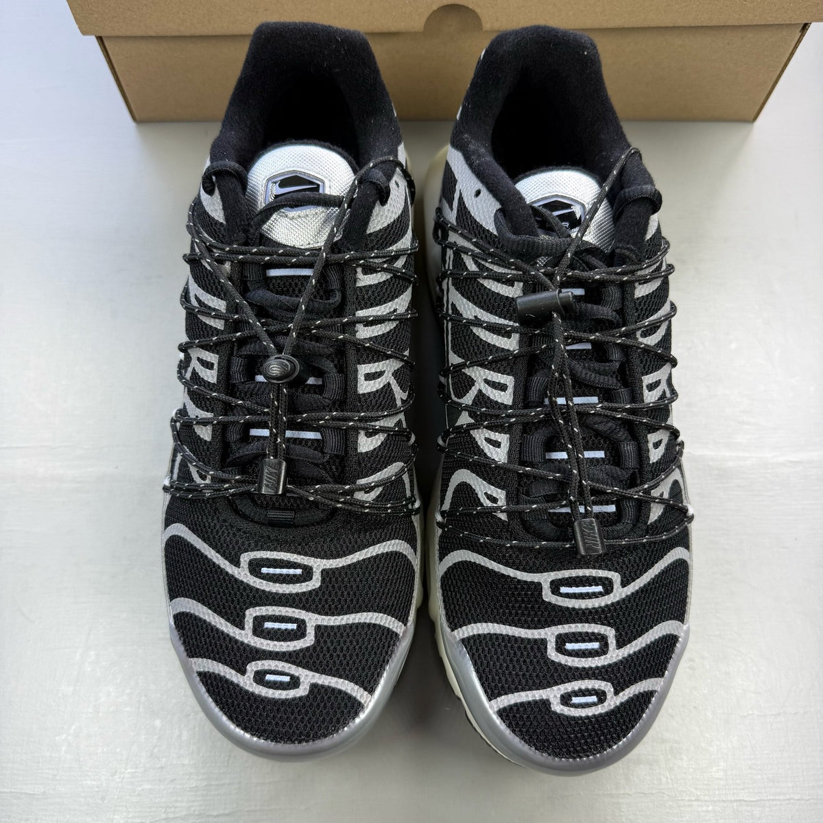 Nike black trainers with silver accents and toggle lacing system.