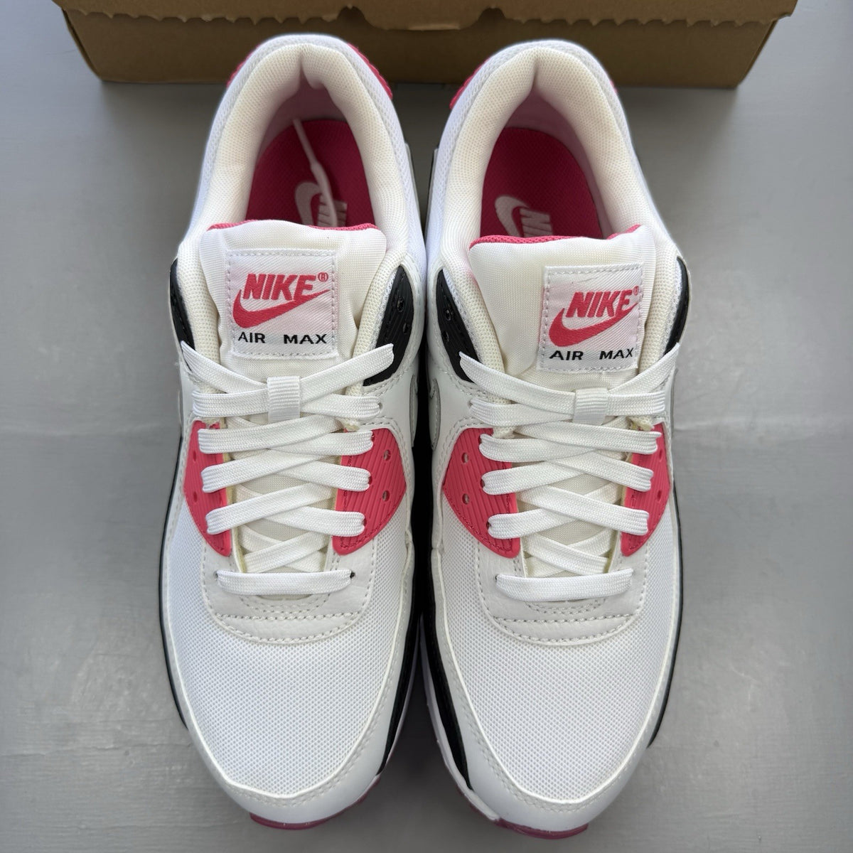 Nike Air Max 90 trainers white with pink and black accents, featuring logo details.