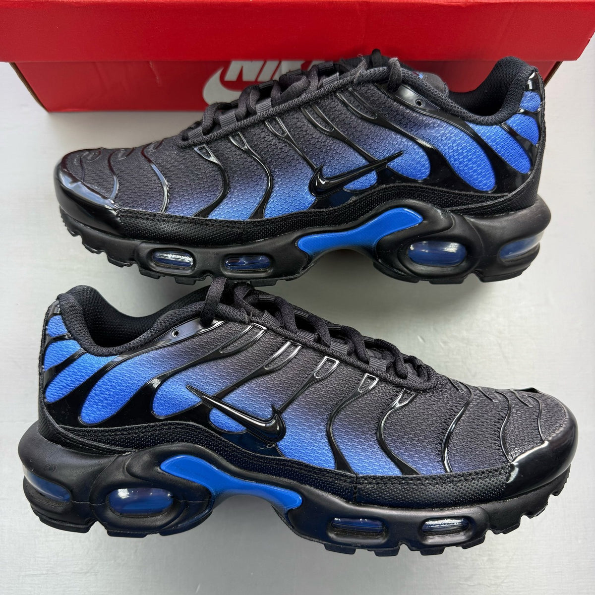 Nike Air Max Plus TN black trainers with blue accents and signature swoosh logo.