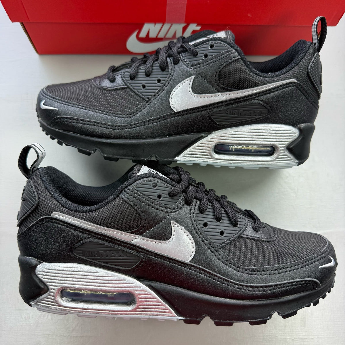 Nike black trainers with metallic silver swoosh logo and sleek design.