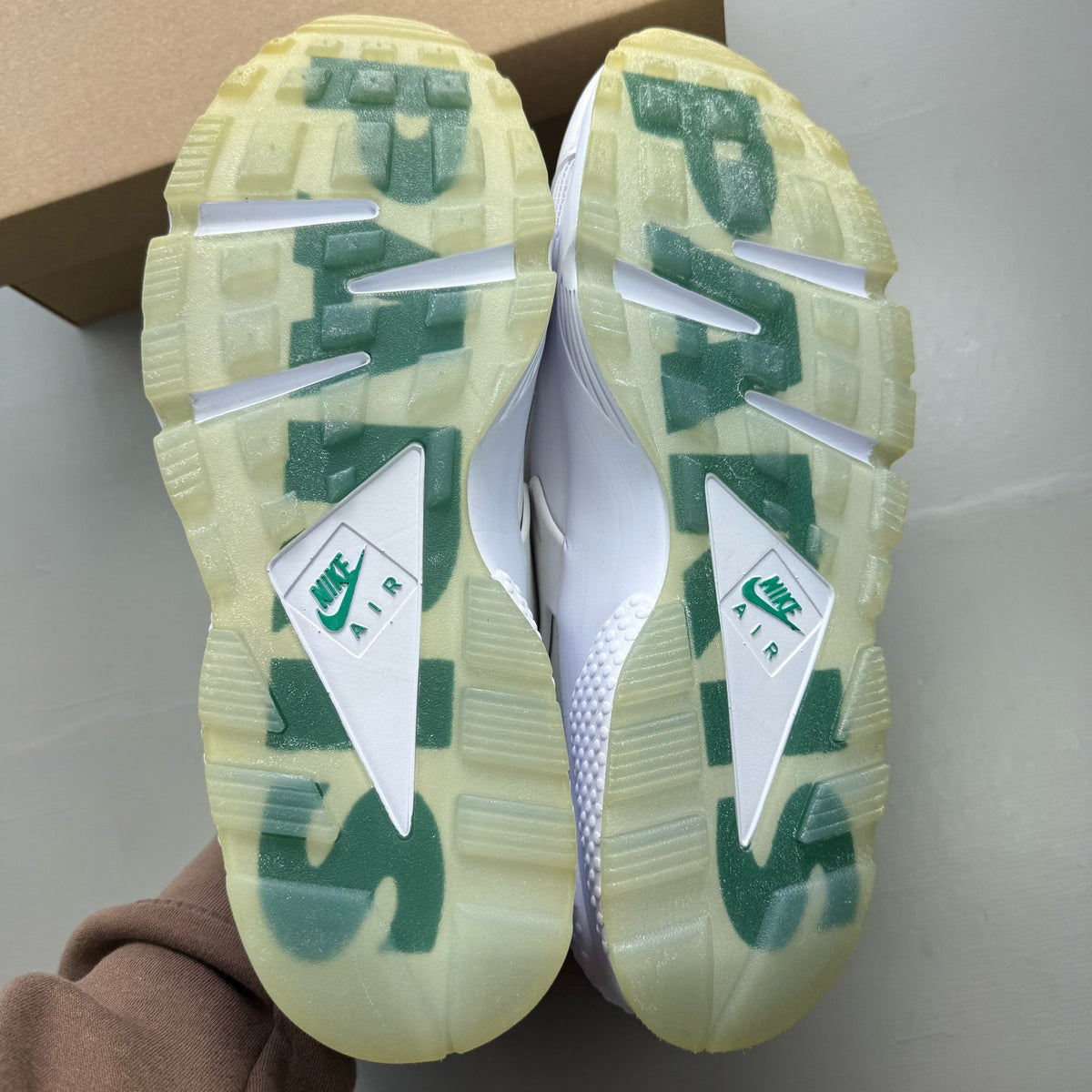 Nike Air Huarache white trainers with green accents and distinctive logo detailing.