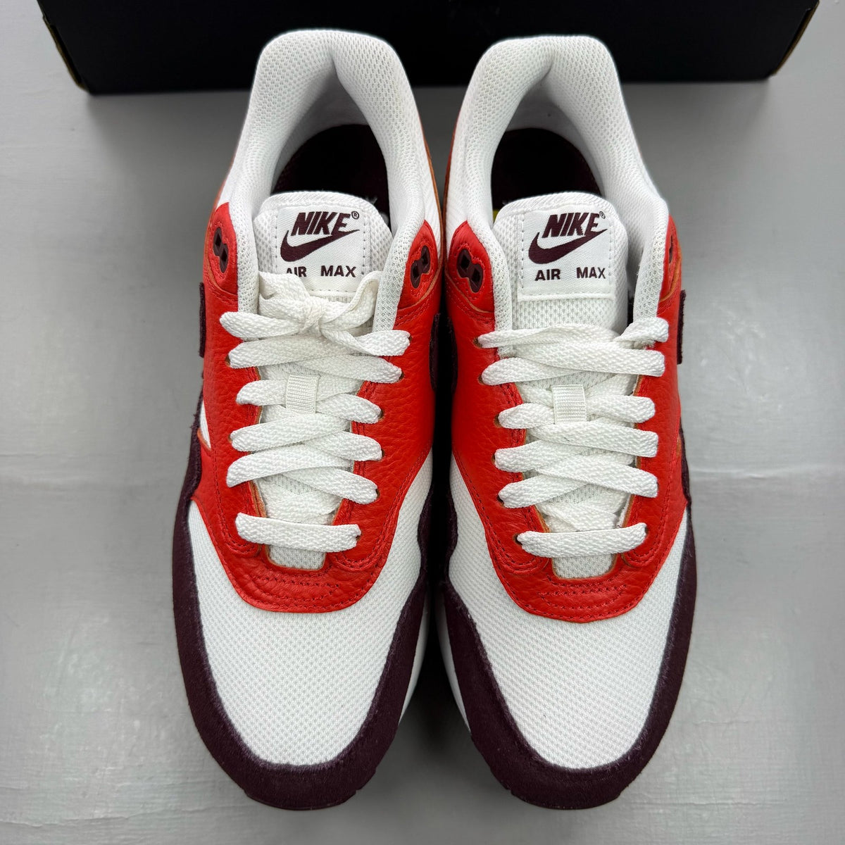 Nike Air Max 1 red trainers with white accents and logo detailing.