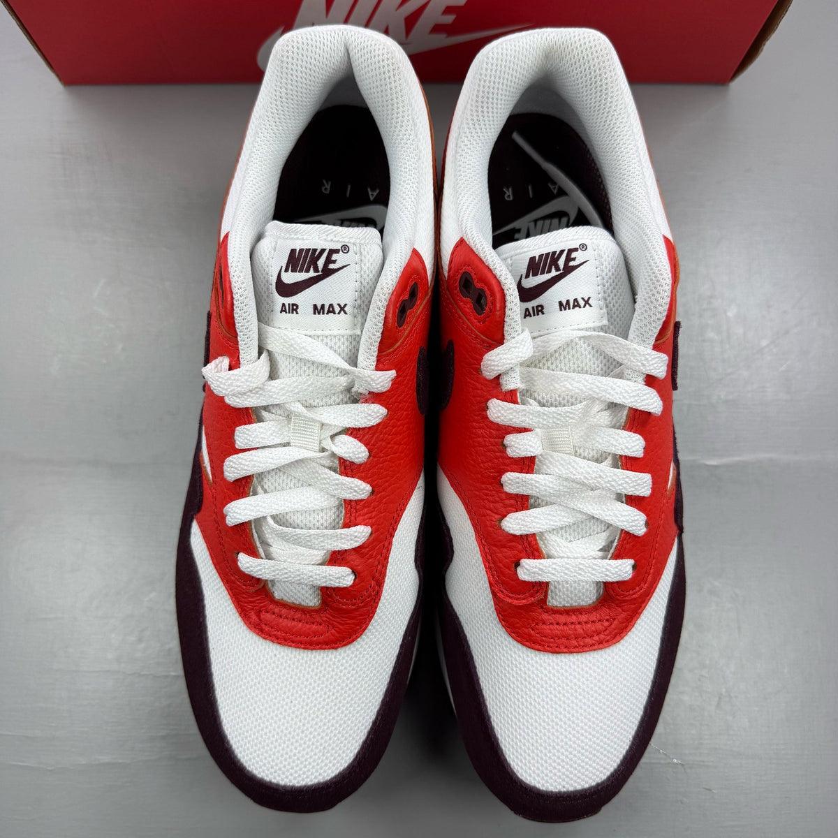 Nike Air Max 1 white trainers with burgundy accents and logo detailing.