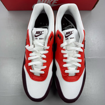 Nike Air Max 1 white trainers with burgundy accents and logo detailing.