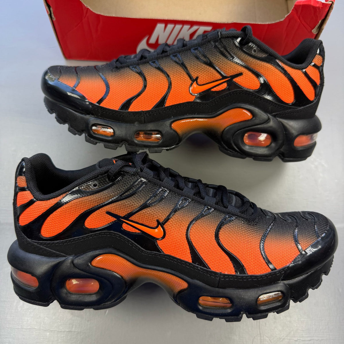 Nike Air Max Plus TN black trainers with orange accents and signature logo details.
