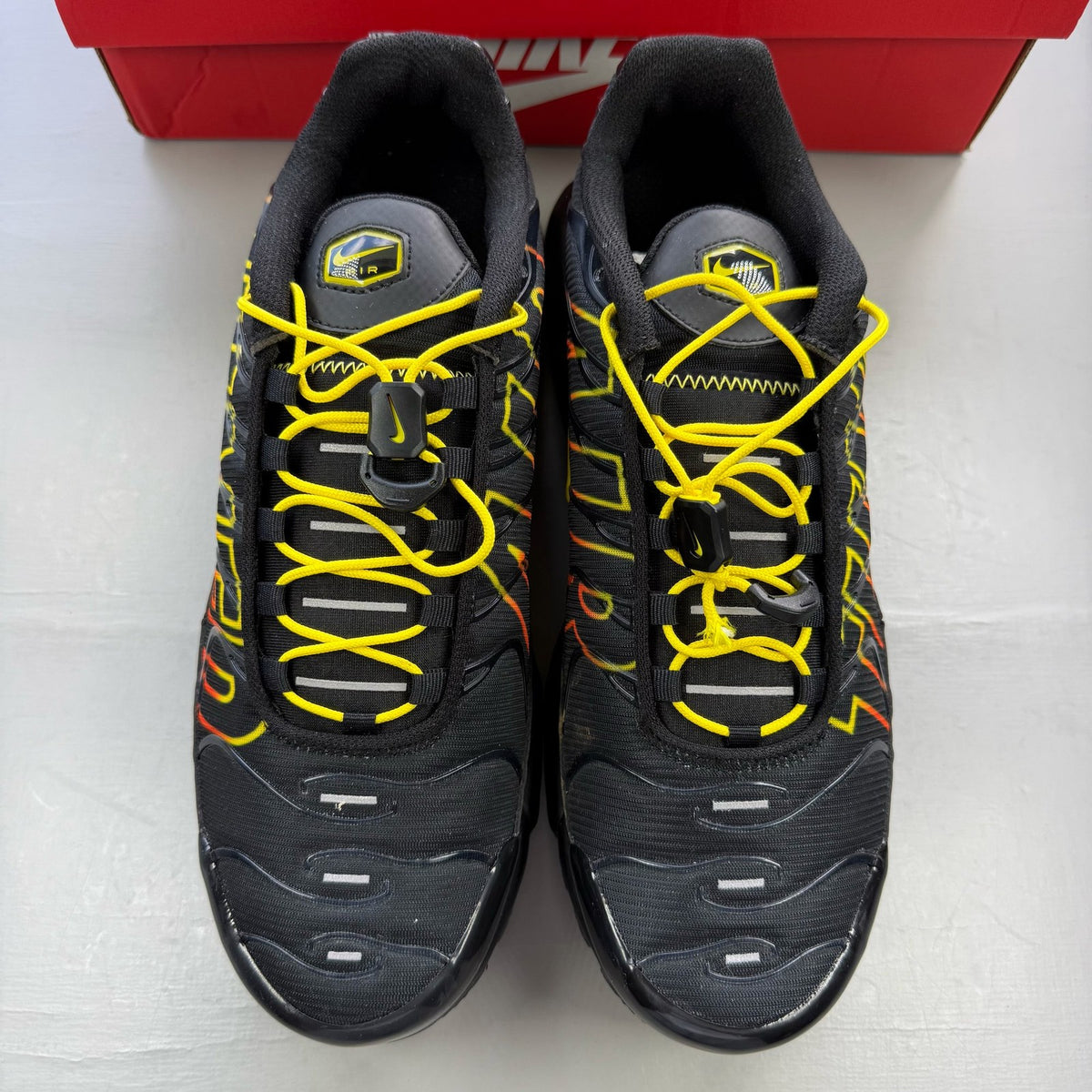 Nike Air Max Plus TN black trainers with signature logo and vibrant sunrise detailing.