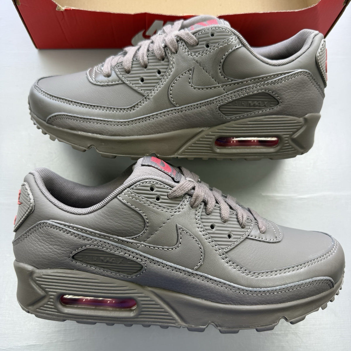 Nike Air Max 90 trainers grey with red accents and logo detail.