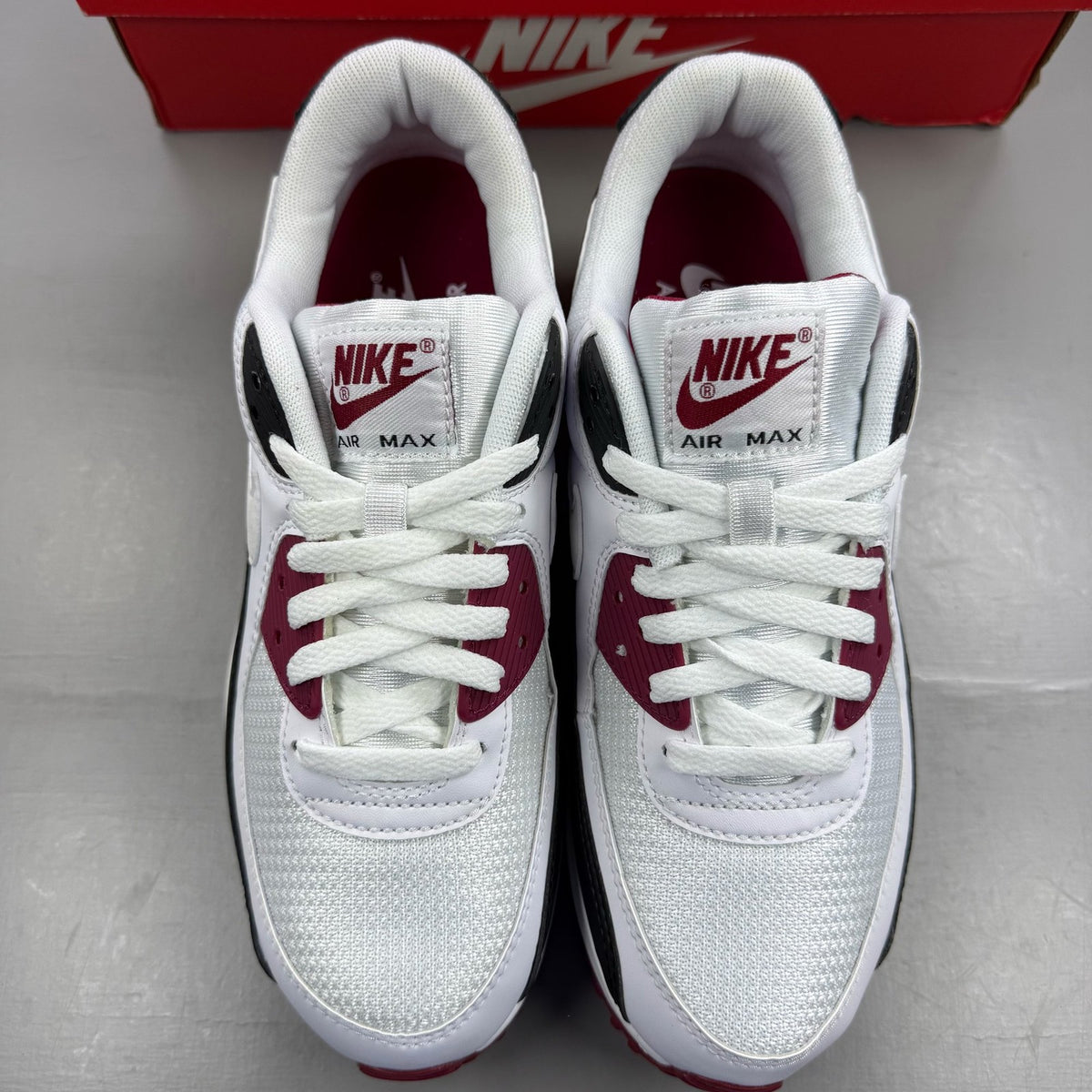 Nike Air Max 90 Recraft white trainers with maroon accents and logo detail.