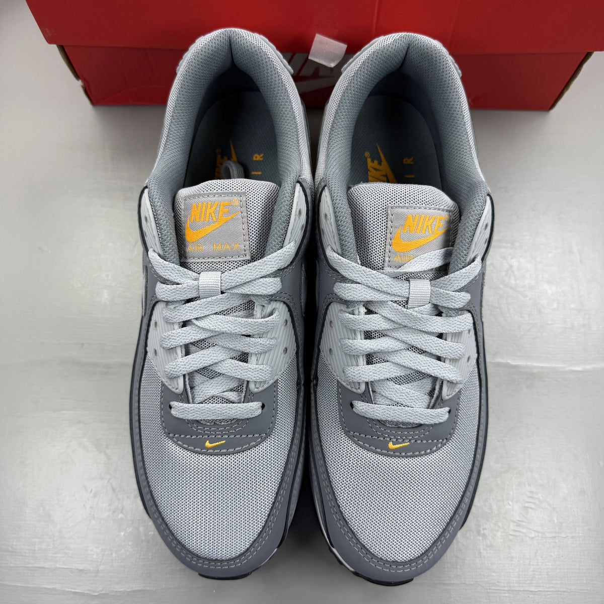 Nike Air Max 90 grey trainers with black and sundial accents, featuring logo details.