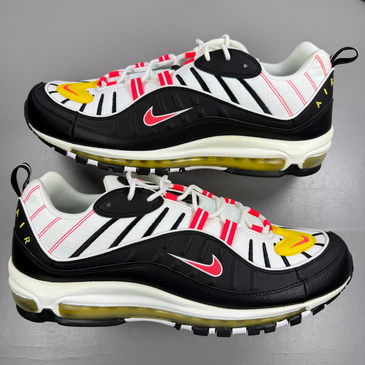 Nike Air Max 98 white trainers with black and yellow accents, featuring a sleek design.
