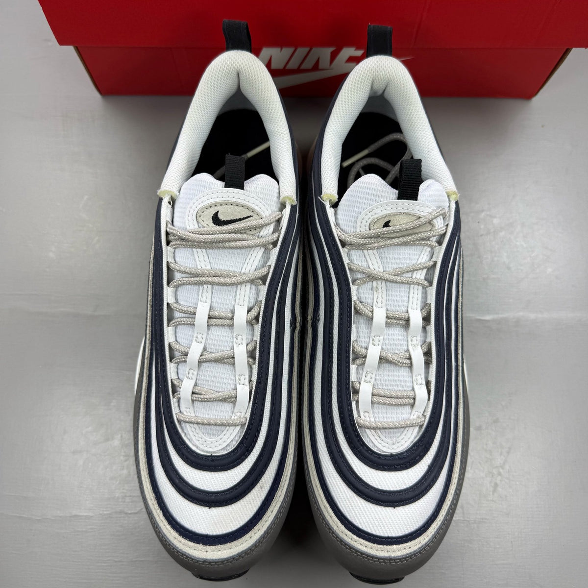 Nike Air Max 97 white trainers with grey and navy accents, featuring iconic swoosh logo.