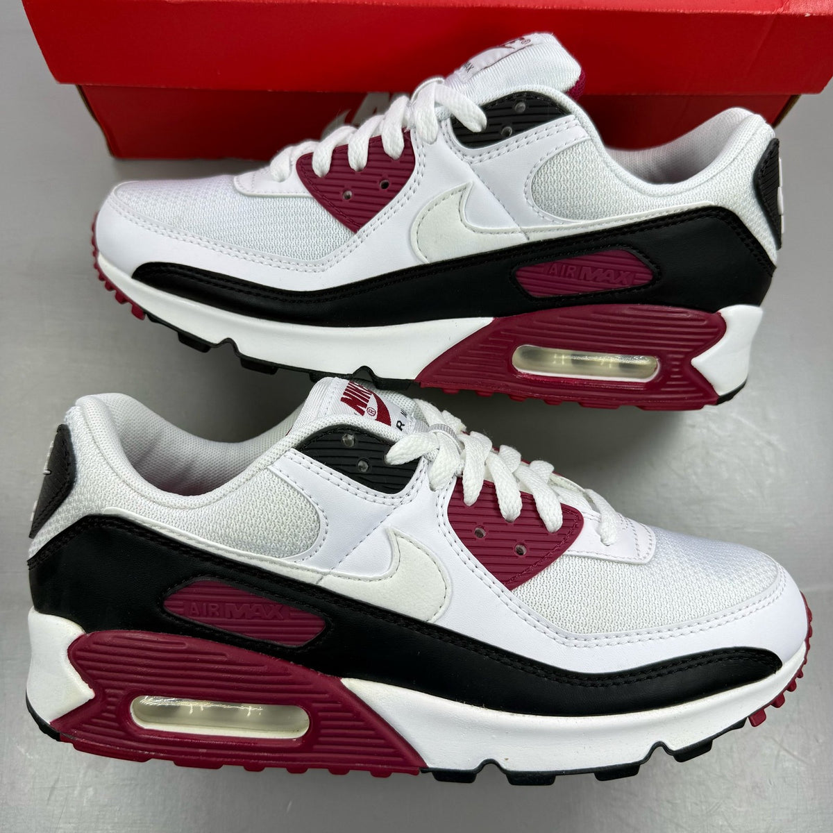 Nike Air Max 90 Recraft white trainers with maroon accents and logo detail.