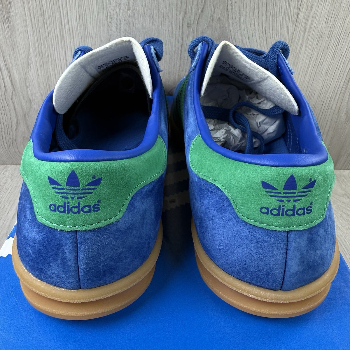 Adidas blue trainers with gum sole and iconic three-stripe logo design.