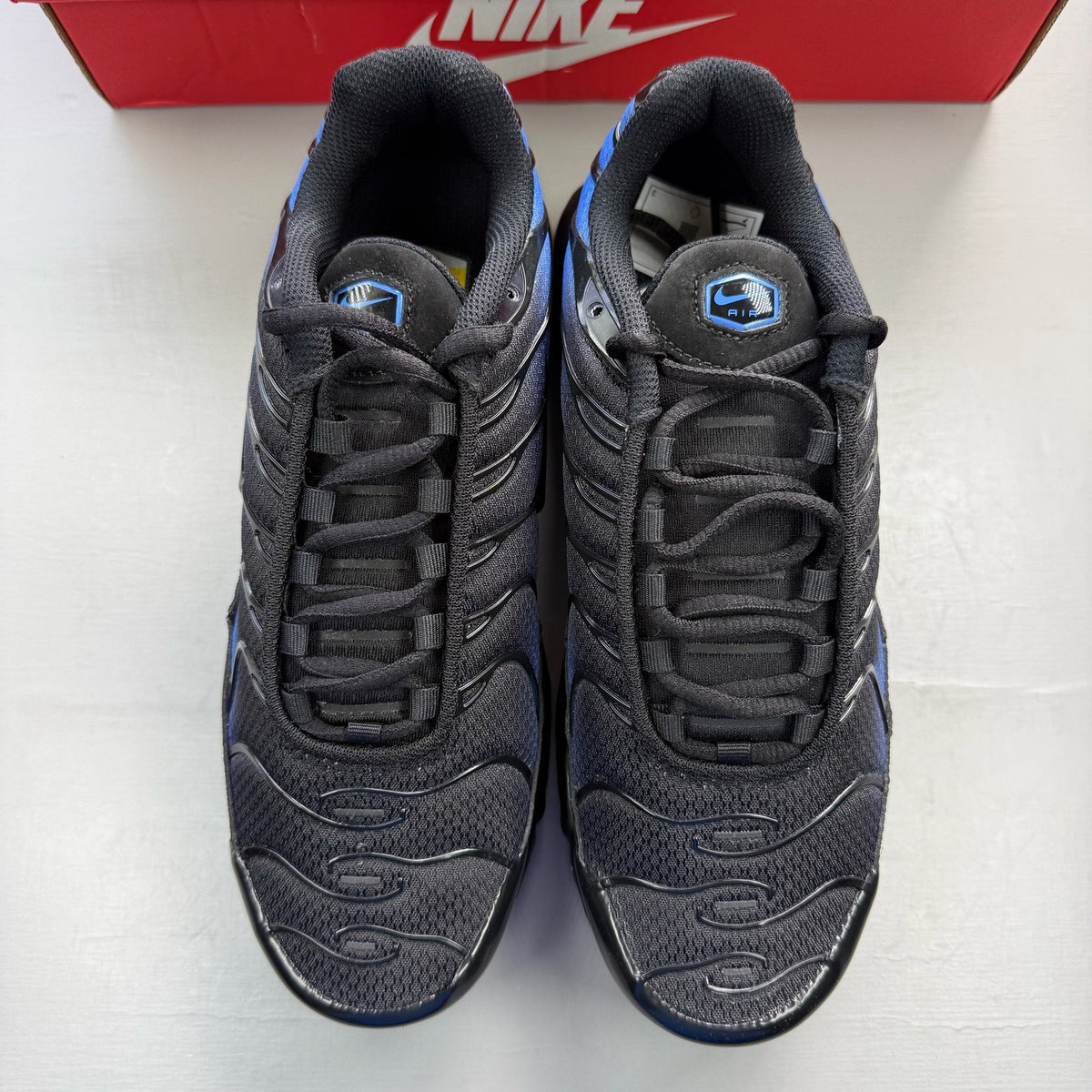 Nike Air Max Plus TN black trainers with blue accents and signature swoosh logo.