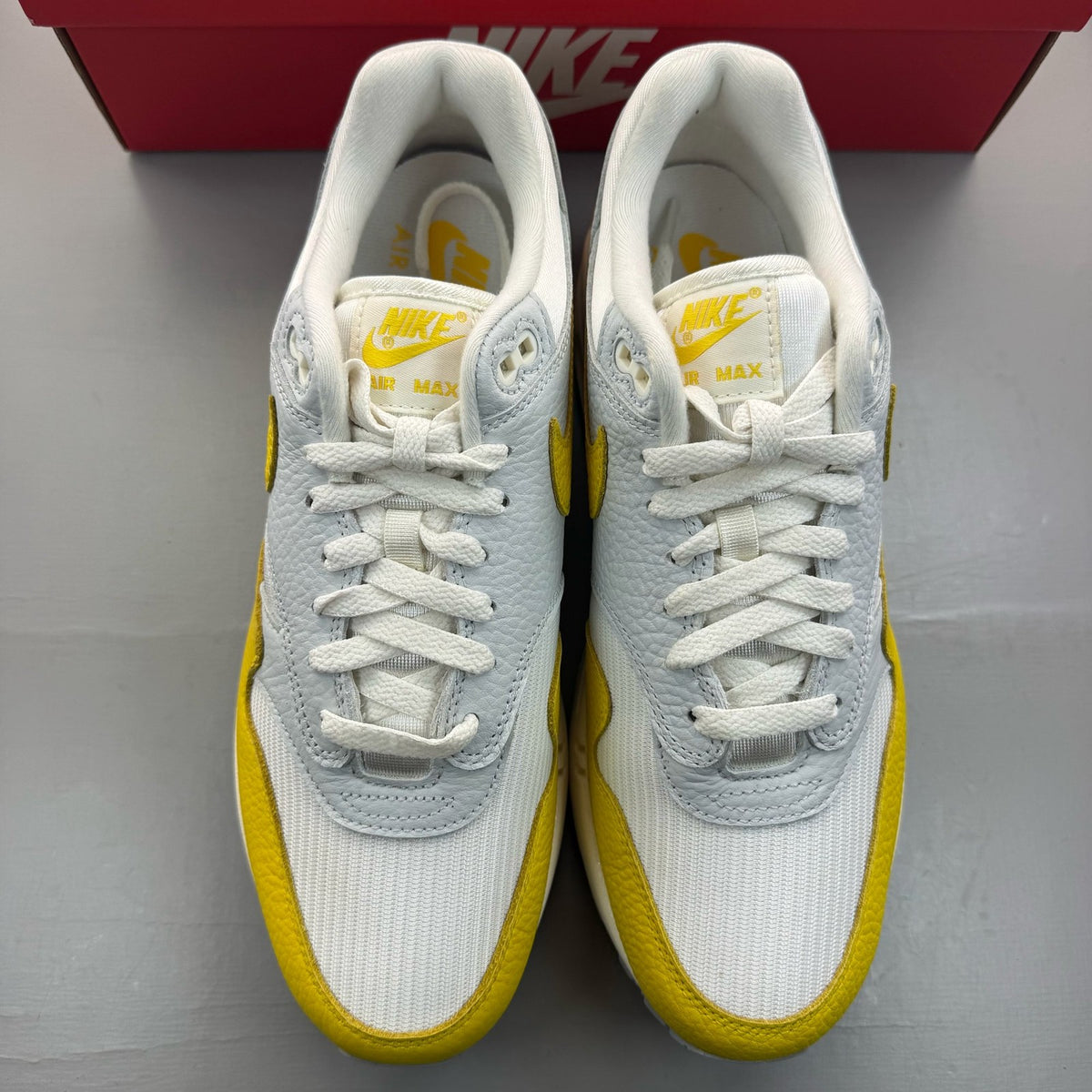 Nike Air Max 1 white trainers with tour yellow accents and logo detail.