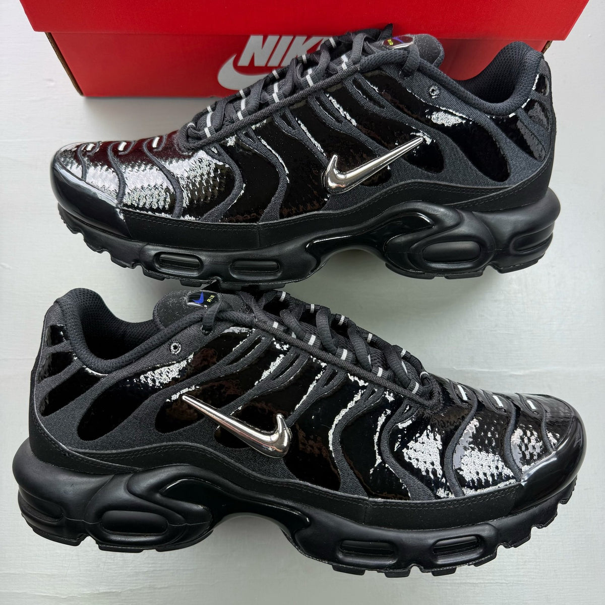 Nike black Air Max Plus TN trainers with chrome accents and vibrant volt detailing.