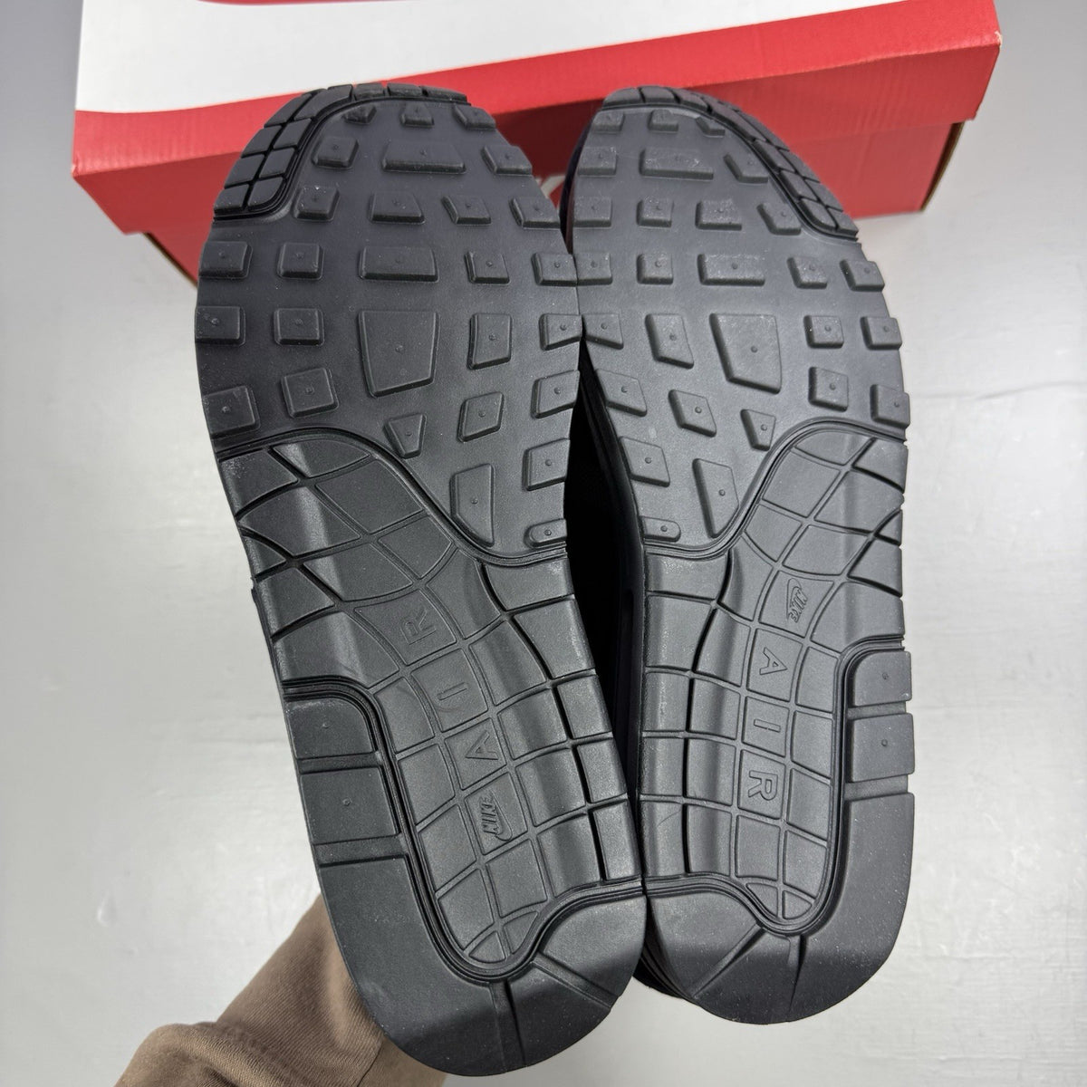 Nike Air Max 1 trainers black with red accents and logo detail on the side.