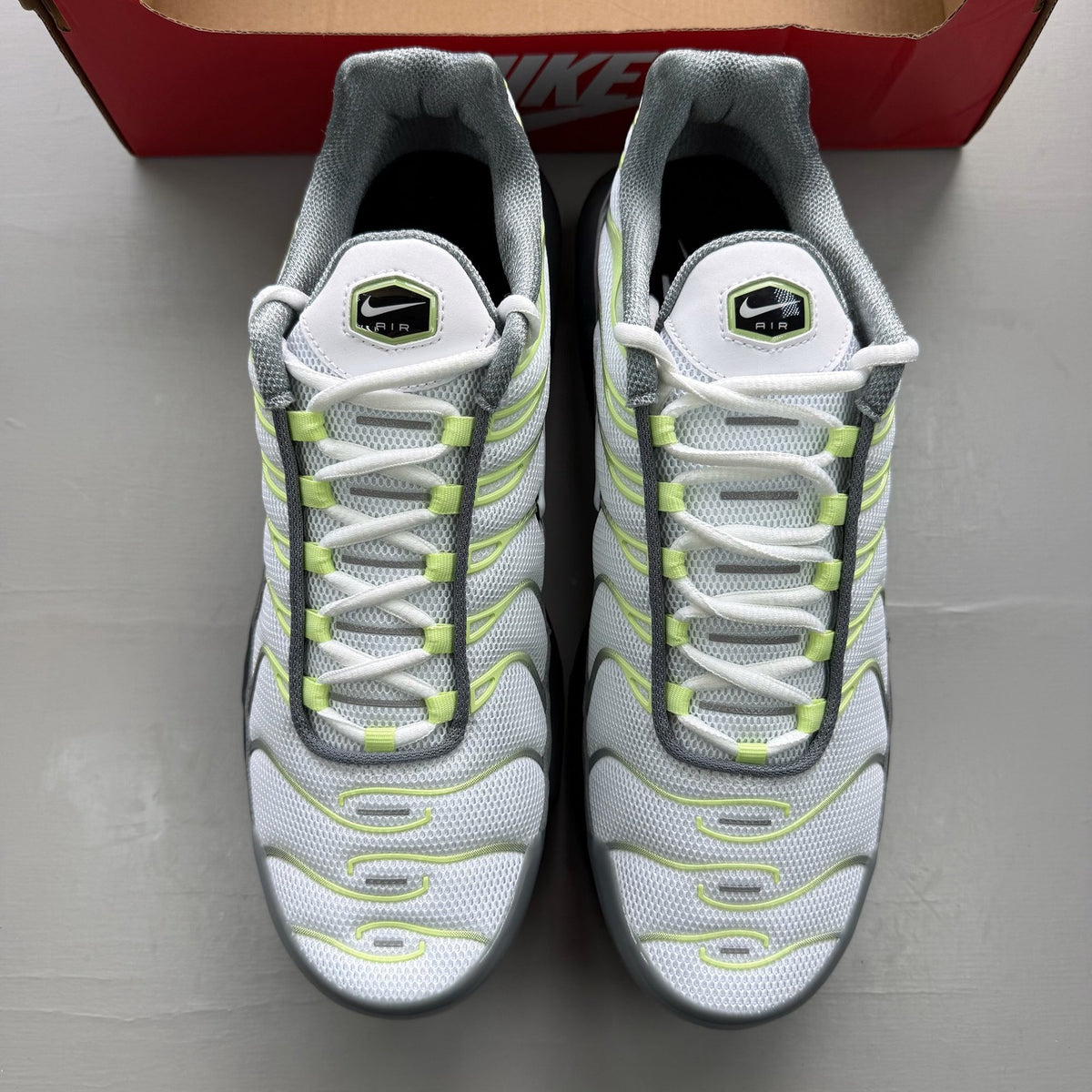 Nike Air Max Plus TN grey trainers with white and liquid lime accents, featuring logo details.