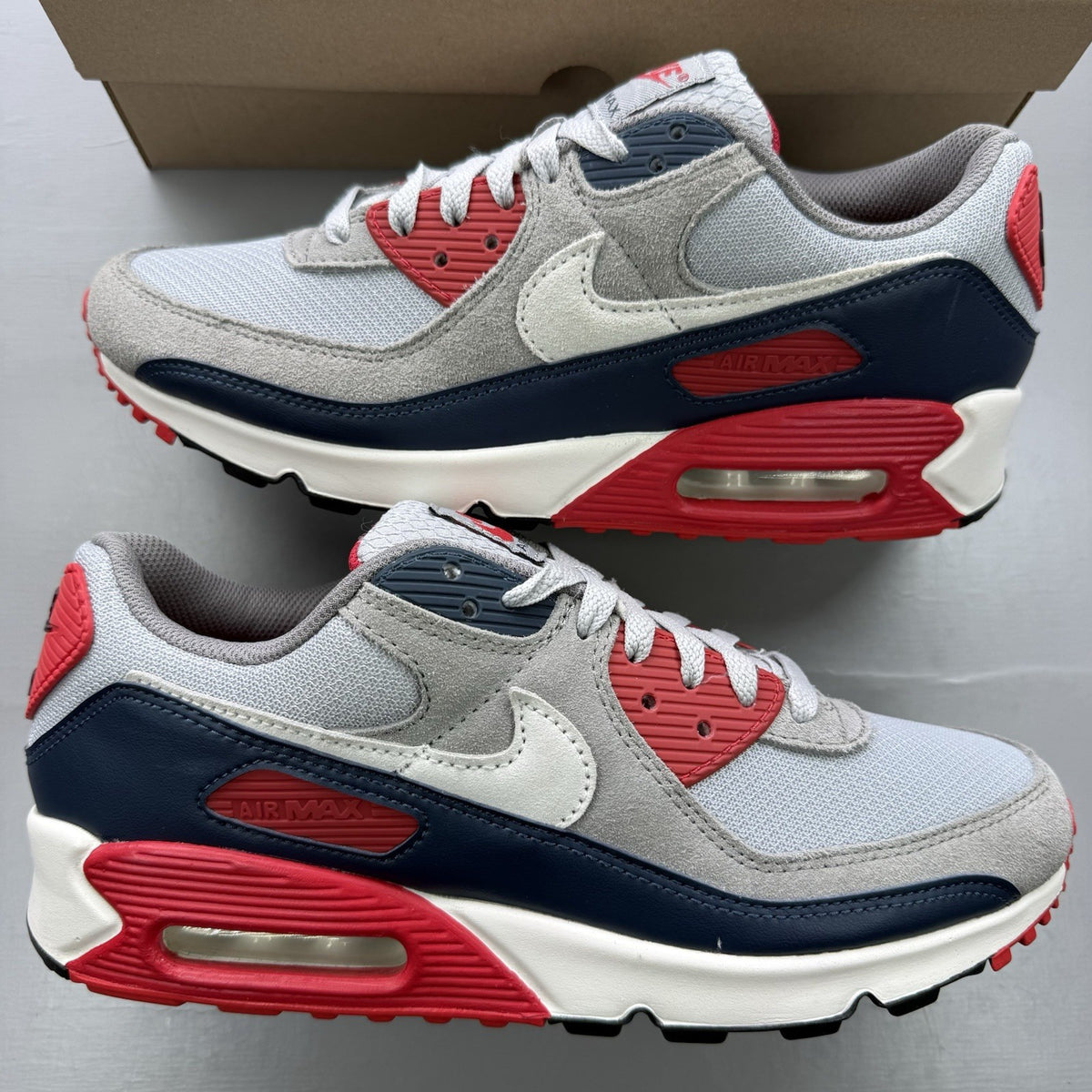 Nike Air Max 90 trainers white with red and navy accents, featuring logo details.