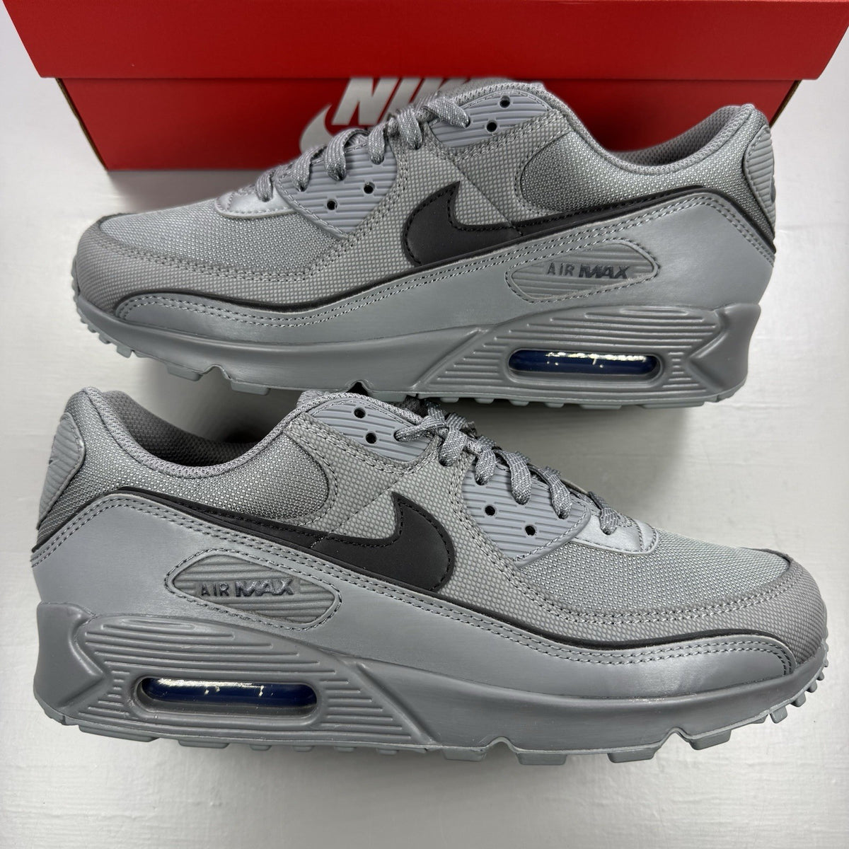 Nike Air Max 90 Premium grey trainers with black accents and signature swoosh logo.