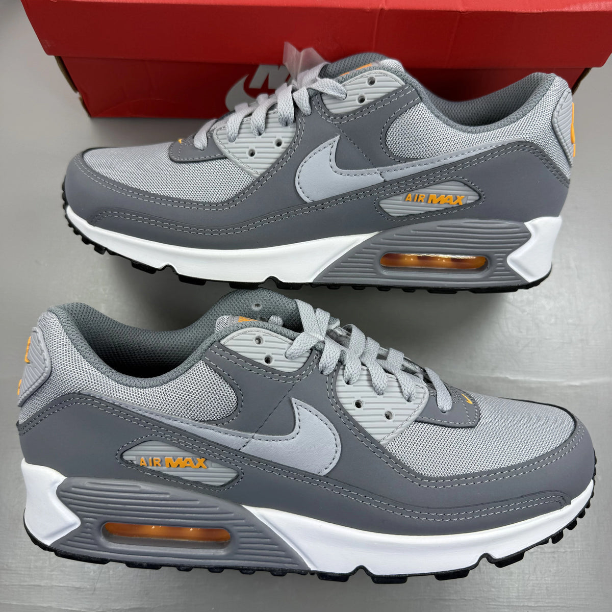 Nike Air Max 90 grey trainers with black and sundial accents, featuring logo details.